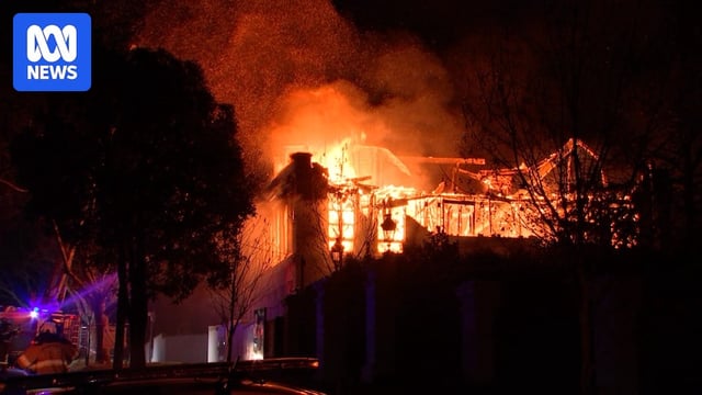 Fire engulfs a large double storey home with flames leaping into the air at night.