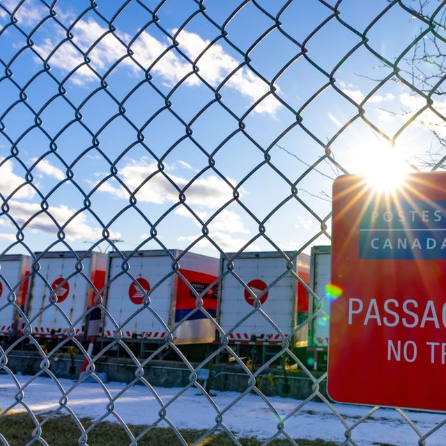 Canada Post trucks are seen behind a fence at a distribution centre in Montreal on Friday, Dec.13, 2024. THE CANADIAN PRESS/Christinne Muschi