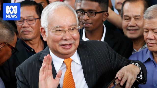Man in glasses surrounded by people waves to camera