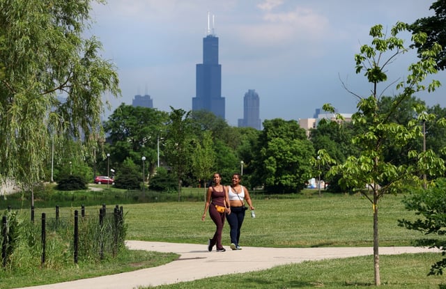 Willis Tower in downtown Chicago is seen in the distance as two women laugh while strolling through Humboldt Park on June 19, 2025.  Temperatures are forecasted to reach into the 90s this weekend and into next week. (Chris Sweda/Chicago Tribune)