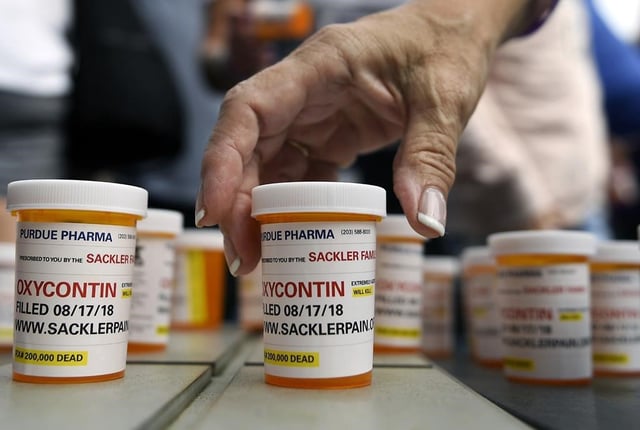 FILE - In this Aug. 17, 2018, file photo, family and friends who have lost loved ones to OxyContin and opioid overdoses leave pill bottles in protest outside the headquarters of Purdue Pharma, which is owned by the Sackler family, in Stamford, Conn. Purdue and state, local and Native American tribal governments across the U.S. agreed to settle lawsuits over the toll of opioids more than a year ago, but the money isn't flowing yet because of a wait for a key court ruling. (AP Photo/Jessica Hill, File)