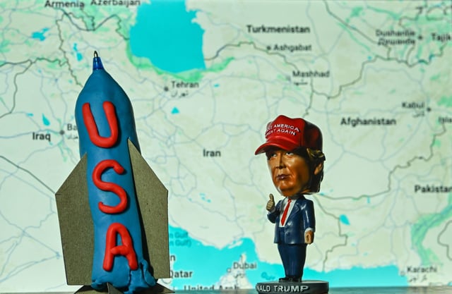 A miniature statue of U.S. President Donald Trump stands beside a model bunker-buster bomb, set against a backdrop featuring a map of the Middle East and Iran, displayed in Kananaskis, Alberta, Canada, on June 19, 2025.
