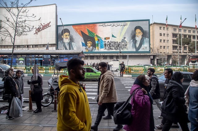 Iranian people walk along the streets in Tehran, Iran, on February 24, 2024. A mural on Enqelab Avenue features the supreme leader of Iran Ali Khamenei, left, soldier Hossein Fahmideh, and the spiritual leader of the Iranian revolution Ayatollah Khomeini.