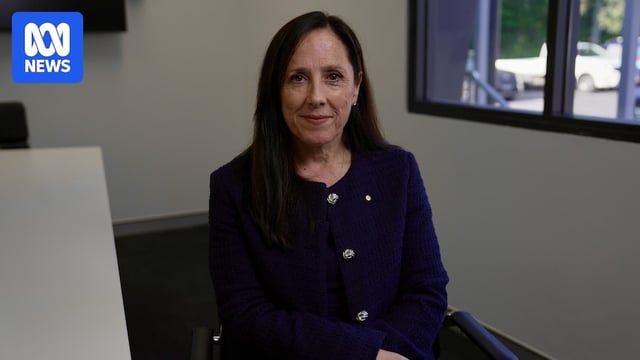 A woman in a purple jacket with large silver buttons sitting in an office chair. 