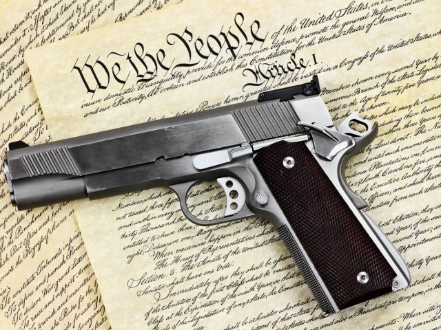 Handgun lying over a copy of the United States constitution with the words "We the People" visible. StephanieFrey/Getty Images