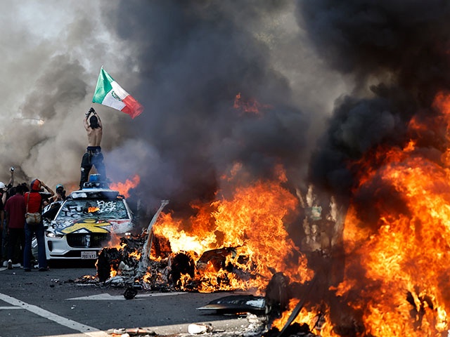 A protestor holds up a Mexican flag as burning cars line the street on June 08, 2025 in Los Angeles, California. Tensions in the city remain high after the Trump administration called in the National Guard against the wishes of city leaders following two days of clashes with police during a series of immigration raids. (Photo by Mario Tama/Getty Images)