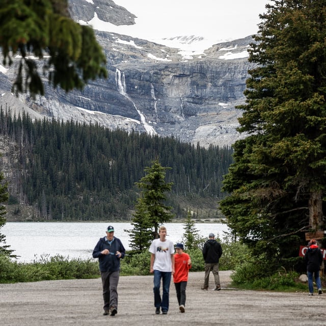 Tourists walk around Bow Lake on Friday, June 20, 2025, near Bow Glacier Falls, seen in background, where a rock slide, light grey area on cliff face, killed two hikers and injured three more Thursday, north of Lake Louise, Alta., in Banff National Park. THE CANADIAN PRESS/Jeff McIntosh