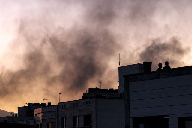 People stand on a rooftop amidst billowing smoke following an overnight Israeli strike in Tehran on June 17.