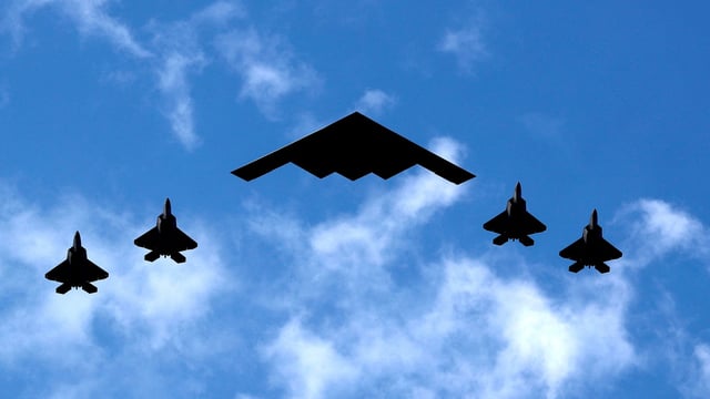 A U.S. Air Force B-2 Spirit Stealth Bomber (C) is flanked by 4 U.S. Marine Corps F-35 fighters 