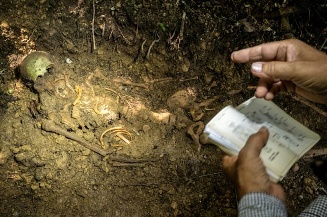 Takamatsu Gushiken, a volunteer who recovers the remains of war dead to be reunited with their families, points at the skeletal remains of a person who died in the Battle of Okinawa during World War II, at a forest in Itoman