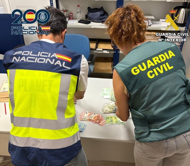 Un policía nacional y una guardia civil recuentan el dinero intervenido en los registros en Xàtiva y La Granja de la Costera.