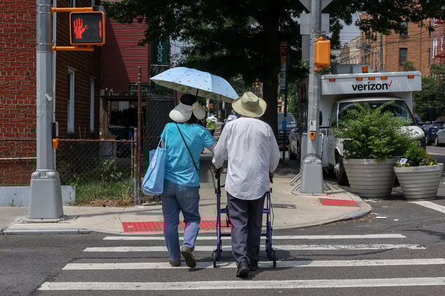 A couple in sun hats and with an umbrella cross the street as an extreme heat warning is in effect in Queens, New York City, U.S., June 23, 2025. REUTERS/Kylie Cooper