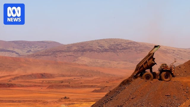 A dump truck emptying a pile of red dirt into a very large mine - there are hills in the background.