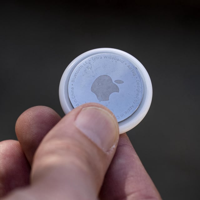 An Apple AirTag held in a person's hand.