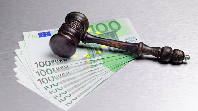 Holzhammer liegt auf mehreren 100-Euro-Scheinen auf metallischer Oberfläche.