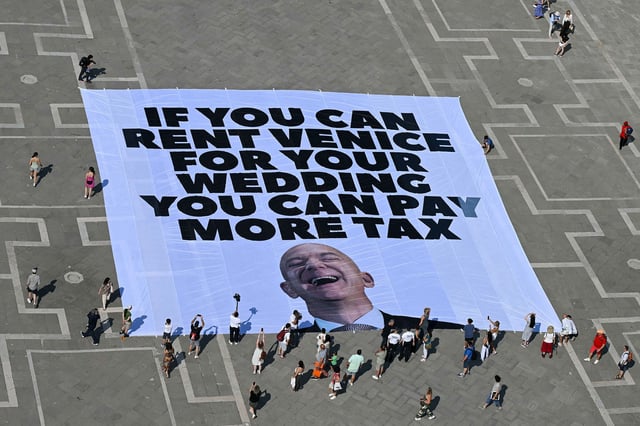Activists of international environmental group Greenpeace deploy a giant banner displaying a picture of Jeff Bezos and reading "If you can rent Venice for your wedding you can pay more tax" at St Mark square  in Venice on June 23, 2025. Venice will host the wedding of Amazon Founder and CEO Jeff Bezos and journalist Lauren Sanchez before the end of the month with more than 200 guests expected to attend. (Photo by Stefano Rellandini / AFP) (Photo by STEFANO RELLANDINI/AFP via Getty Images)          