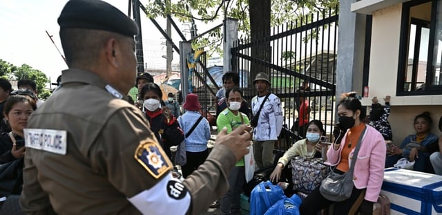 Un policier thaïlandais échange avec des personnes qui attendent de traverser le poste-frontière international de Ban Khlong Luek entre la Thaïlande et le Cambodge, dans le district d'Aranyaprathet,  en Thaïlande, le 24 juin 2025