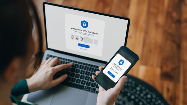 Eine Person hält ein Smartphone und benutzt gleichzeitig einen Laptop. Auf dem Laptopbildschirm ist eine Authentifizierungsaufforderung mit dem Text Authenticate Your Account und Eingabefeldern für einen Code zu sehen.