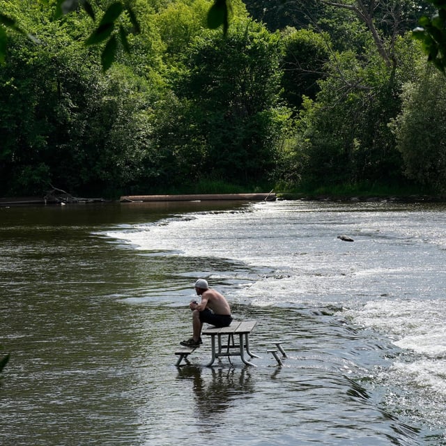 A man cools sits in a picnic table in the waters of the Rideau River in Ottawa on Monday, June 23, 2025. THE CANADIAN PRESS/Adrian Wyld