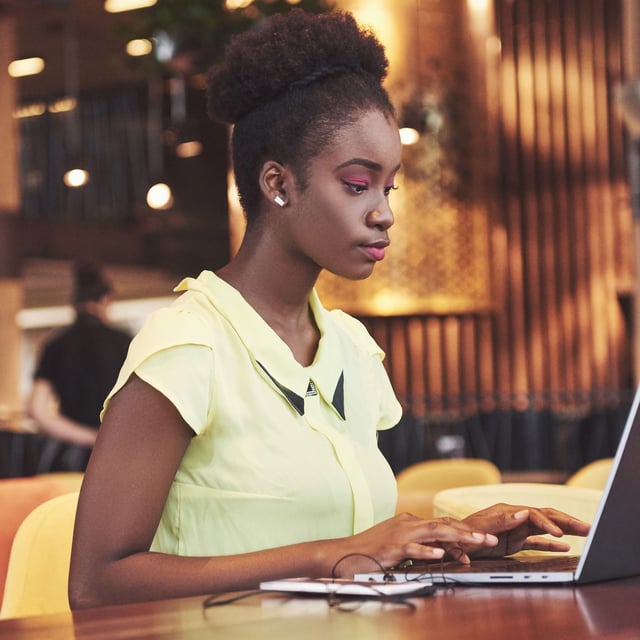 A woman sitting at a table and using a laptop with her phone nearby