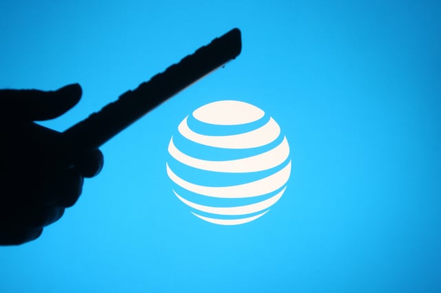 UKRAINE – 2021/03/04: In this photo illustration the AT&amp;T logo is seen behind a silhouette hand holding a tv remote. (Photo Illustration by Pavlo Gonchar/SOPA Images/LightRocket via Getty Images)