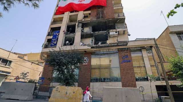 A woman walks past a residential building that was hit in an Israeli strike covered with a big Iranian flag, in Tehran on June 25, 2025. A fragile ceasefire in the Iran-Israel war appeared to be holding on June 25, after 12 days of strikes that saw Israel and the United States pummel the Islamic republic’s nuclear facilities. (Atta Kenare/AFP/Getty Images/TNS)