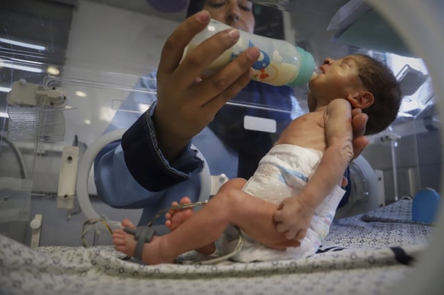 A nurse feeds a prematurely born baby lying in an incubator at the neonatal intensive care unit of Nasser Hospital in Khan Younis, southern Gaza Strip, Thursday, June 19, 2025. (AP Photo/Mariam Dagga)