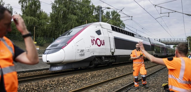 Un TGV Inoui passe près de techniciens de la SNCF qui travaillent à reconnecter les câbles ferroviaires à la gare de Mont-de-Terre à Lille, le 25 juin 2025 dans le Nord