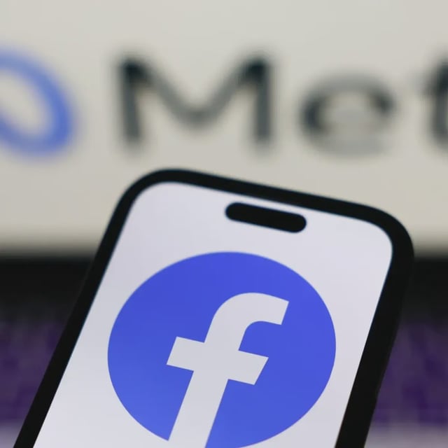 The Facebook logo on a phone with a laptop featuring "Meta" behind.