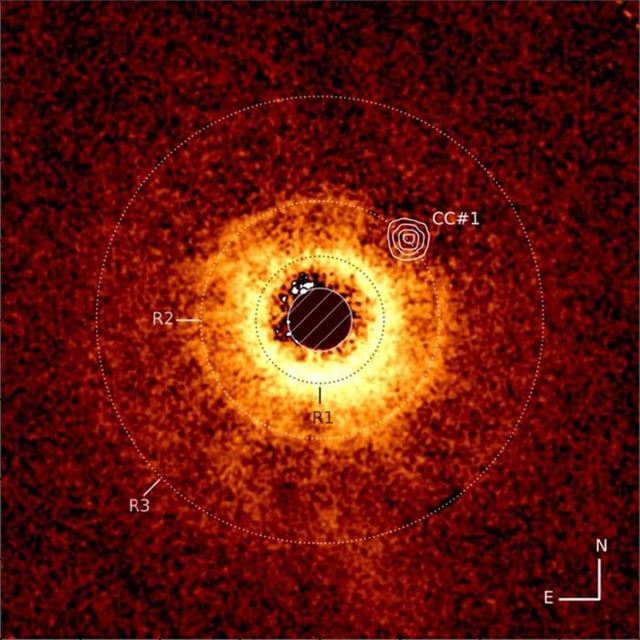 Sur cette photo prise par le télescope James-Webb, la surface de l'étoile TWA 7 est masquée en noir, ce qui permet de mieux voir la matière chaude (jaune-rouge) qui l'entoure. En haut à droite (dans les cercles concentriques), un trou apparent dans cette matière marque l'emplacement d'une planète.