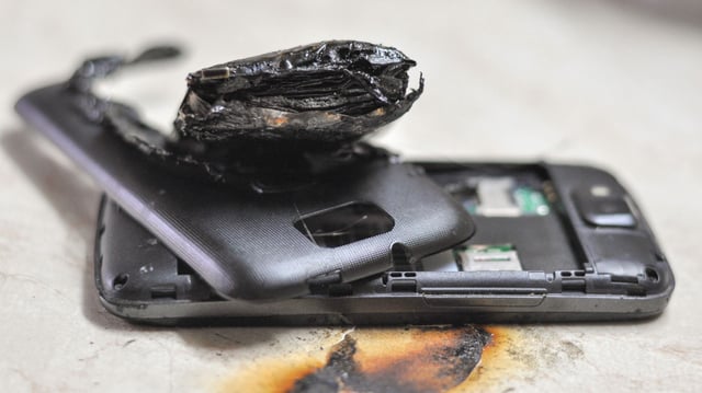 A severely damaged smartphone with its casing blown open and battery charred after a lithium-ion cell failure. The burn marks and internal destruction illustrate the dangerous outcome of thermal runaway, a catastrophic event that the new ultrasound-based diagnostic tool aims to prevent by detecting defects inside batteries before such failures occur.