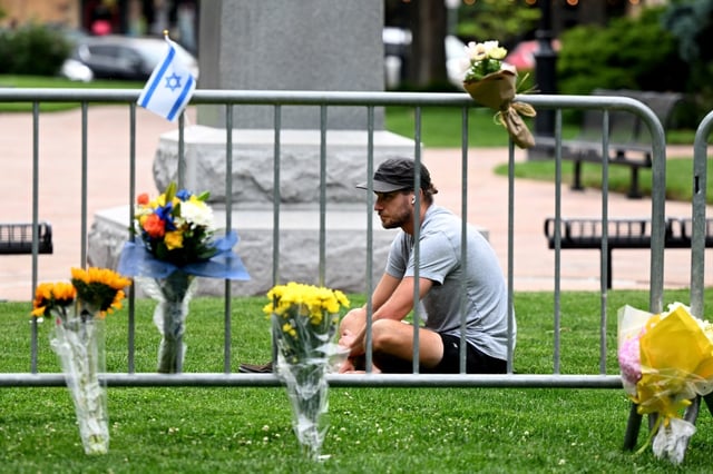 Connor Russell sits on the grass next to flowers and a flag that have been left on fencing next to the scene of Sunday’s attack on the Pearl Street Mall in Boulder on Monday, June  2, 2025. Russell, a Boulder resident, said he came to the site to help him process what happened. “I have been having a hard time understanding how this happened here,” he said. (Photo by Helen H. Richardson/The Denver Post)