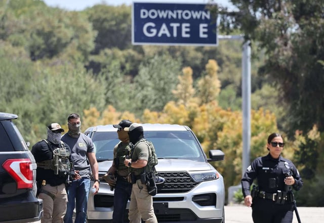An LAPD officer walks near masked federal agents staged outside a gate of Dodger Stadium on June 19. The Los Angeles Dodgers said in a statement that federal agents requested permission to access Dodger Stadium parking lots but were denied entry. (Photo by Mario Tama/Getty Images)
