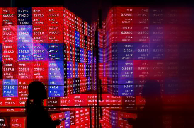 A visitor stands next to an electronic screen displaying Japan's Nikkei stock prices quotation board as the average surged past an all-time record high scaled in December 1989, inside a building in Tokyo, Japan February 22, 2024.  REUTERS/Issei Kato/File Photo