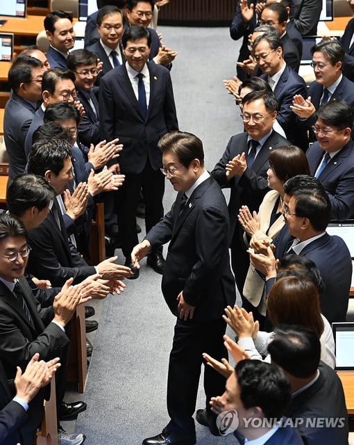 President Lee Jae Myung (C) is applauded by lawmakers of the ruling Democratic Party as he enters a plenary session at the National Assembly in Seoul on June 26, 2025, to deliver a policy speech about a government-proposed extra budget of 20.2 trillion won (US$14.7 billion) aimed at revitalizing domestic consumption and bolstering the economy, including the distribution of cash handouts to all citizens. (Pool photo) (Yonhap)
