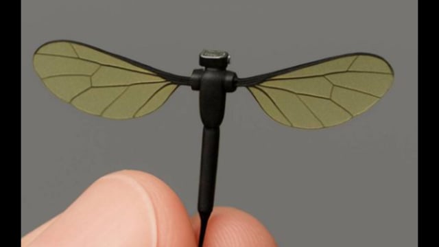The tiny drone has yellow wings like leaves, a thin black body, and three wiry legs, making it look just like a real insect.