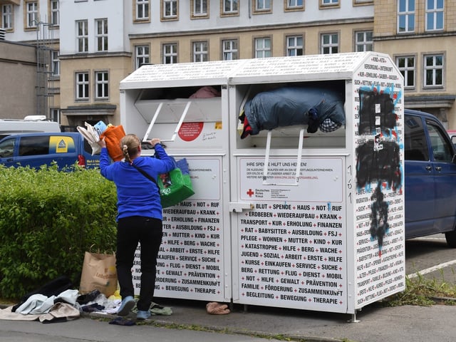 Eine Frau befüllt in Berlin einen Altkleider-Container des Deutschen Roten Kreuzes mit Kleidungsstücken