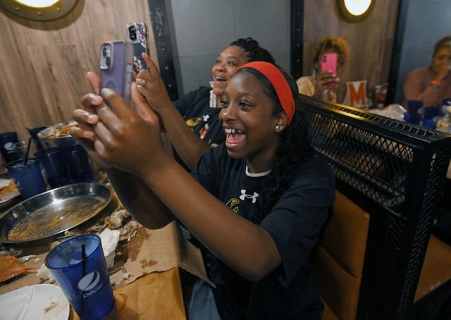 Morgan McNair, 14, of Baltimore, cheers as she takes video of cousin Derik Queen who was announced as the 13th pick in the first round of the NBA 2025 draft during a watch party at the Urban Crab Shack in Parkville. (Kenneth K. Lam/staff)