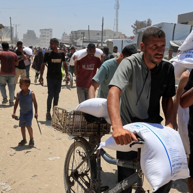 Palestinians carry sacks of flour as they gather to receive aid supplies in Khan Younis, in the southern Gaza Strip, on Thursday.