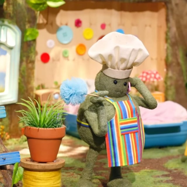 The green tiny chef character wearing a chef's hat and taking a phone call.
