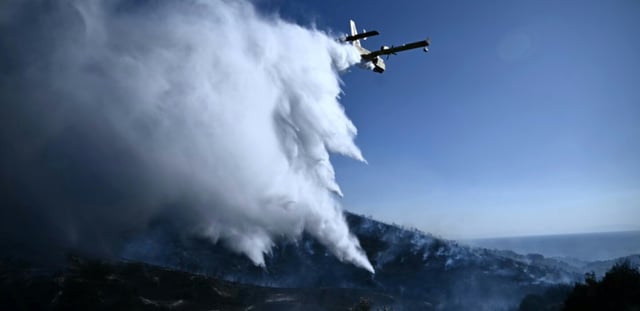 Un avion Canadair de lutte contre les incendies largue de l'eau sur un feu de forêt, près de Thymari, au sud-est d'Athènes, le 26 juin 2025 en Grèce
