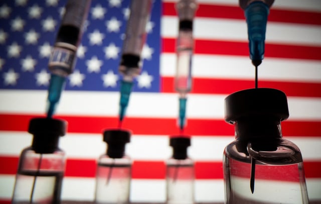 Vials and syringes are seen in front of displayed U.S. flag in this illustration photo taken March 16, 2021. Picture taken March 16, 2021. REUTERS/Dado Ruvic/Illustration