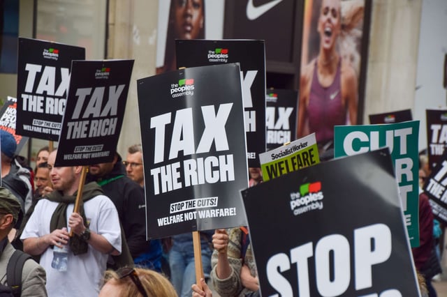 Protesters hold 'Tax the rich' placards during a march against government cuts on June 7, 2025, in London, United Kingdom.