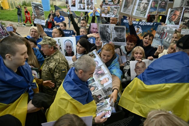 Des prisonniers de guerre ukrainiens libérés enveloppés dans le drapeau national passent devant une foule tenant des portraits de leurs proches et amis disparus ou capturés, à leur arrivée après un échange de prisonniers dans la région de Tcherniguiv, le 26 juin 2025, en Ukraine