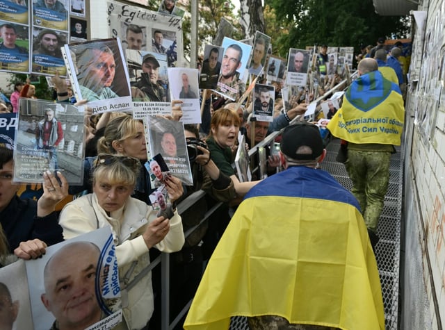 Des prisonniers de guerre ukrainiens libérés enveloppés dans le drapeau national passent devant une foule tenant des portraits de leurs proches et amis disparus ou capturés, à leur arrivée après un échange de prisonniers dans la région de Tcherniguiv, le 26 juin 2025, en Ukraine