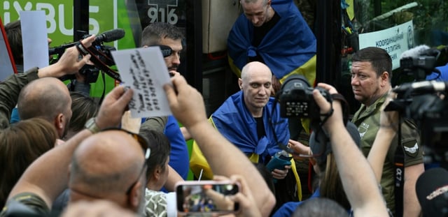 Des prisonniers de guerre ukrainiens libérés enveloppés dans le drapeau national débarquent d'un bus à leur arrivée après un échange de prisonniers dans la région de Tcherniguiv, le 26 juin 2025, en Ukraine