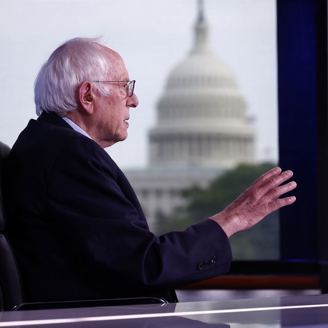 bernie sanders sitting at a desk with the capitol building in the background