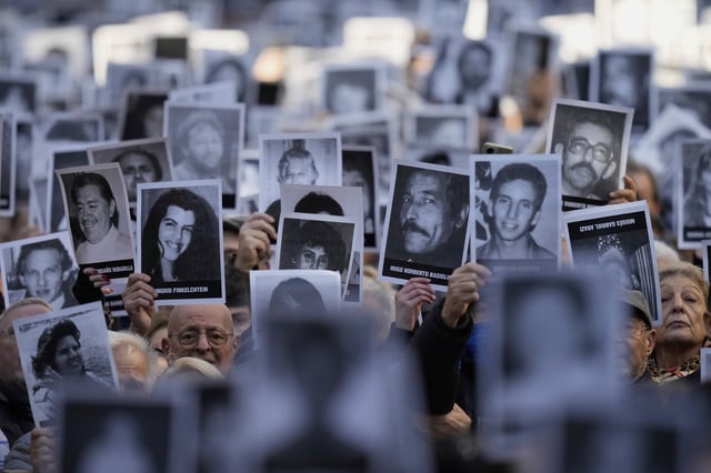 FILE - People hold photos of bombing victims as sirens blare during a ceremony marking the 30th anniversary of the bombing of the AMIA Jewish center that killed 85 people, in Buenos Aires, Argentina, July 18, 2024. (AP Photo/Natacha Pisarenko, File)