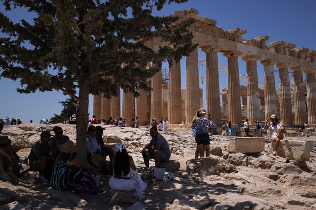 Tourists rest in the shade of a tree during their visit at the Parthenon temple atop the Acropolis hill, as a heatwave hits Athens, Greece, June 27, 2025. REUTERS/Stelios Misinas