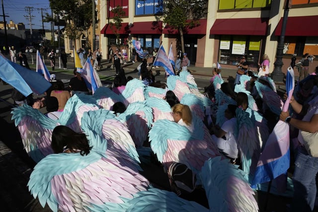 Participants wearing angel wings in the colors of the Transgender Pride flag kneel on the ground during the annual Trans March.